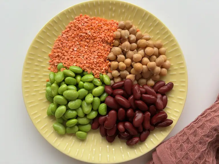 Tallerken med fire forskellige slags bælgfrugter. Der er røde linser, kikærter, edamamebønner og kidneybønner. 
